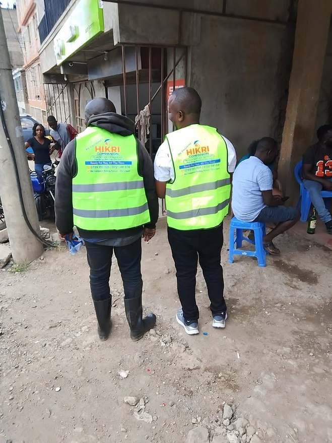 Two field agents in Hikri Companion vests visiting a local shopfront