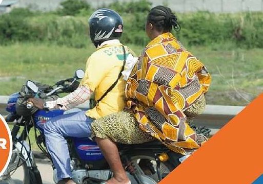 A boda boda rider carrying a passenger on a Kenyan road